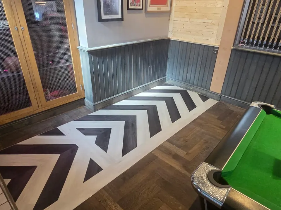 Black and white chevron floor design with a border, set into dark herringbone in a games room