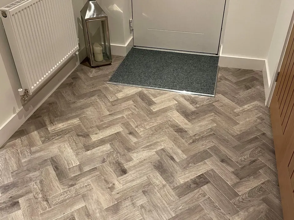 Grey oak-effect herringbone in an entrance hall, cut neatly around an inset doormat