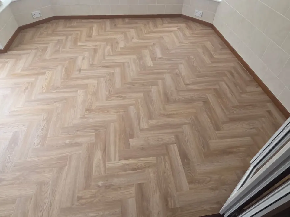 Light oak-effect herringbone flooring laid across a conservatory