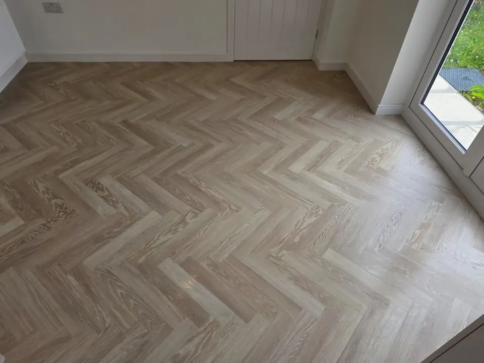 Light ash-effect herringbone flooring in a dining room with garden doors
