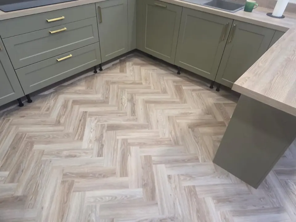 Light oak-effect herringbone flooring in a kitchen with sage green units