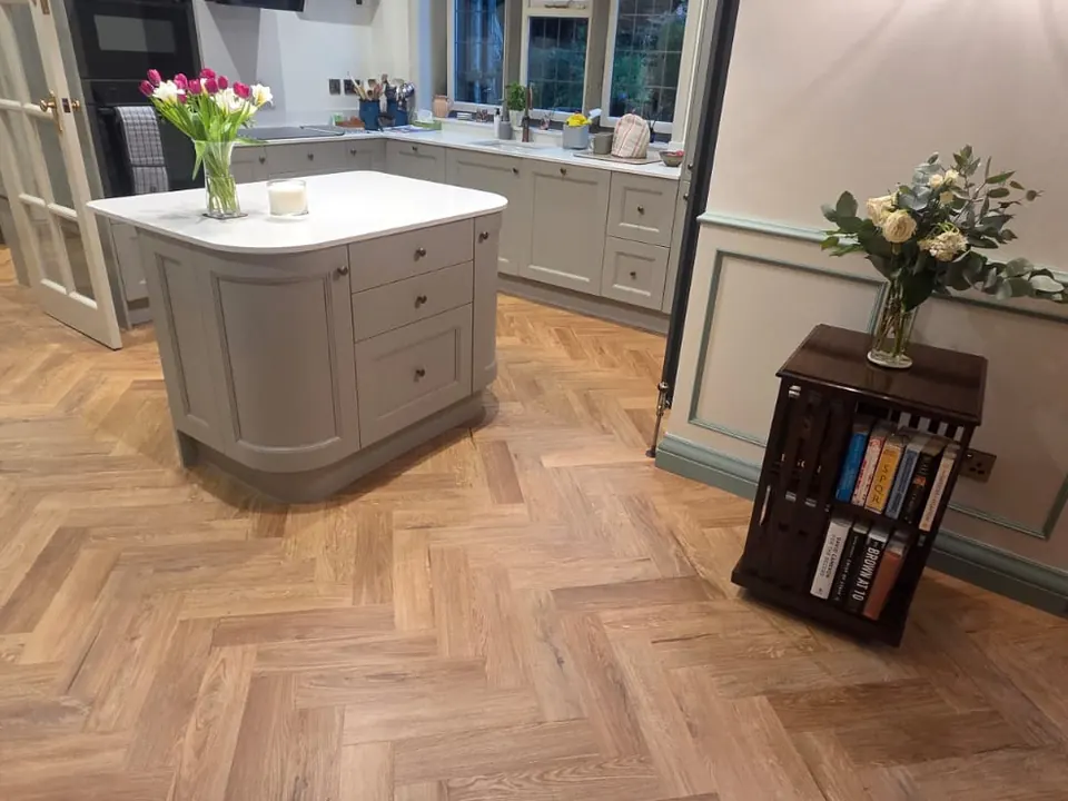 Oak-effect herringbone flooring fitted through a kitchen with a painted island