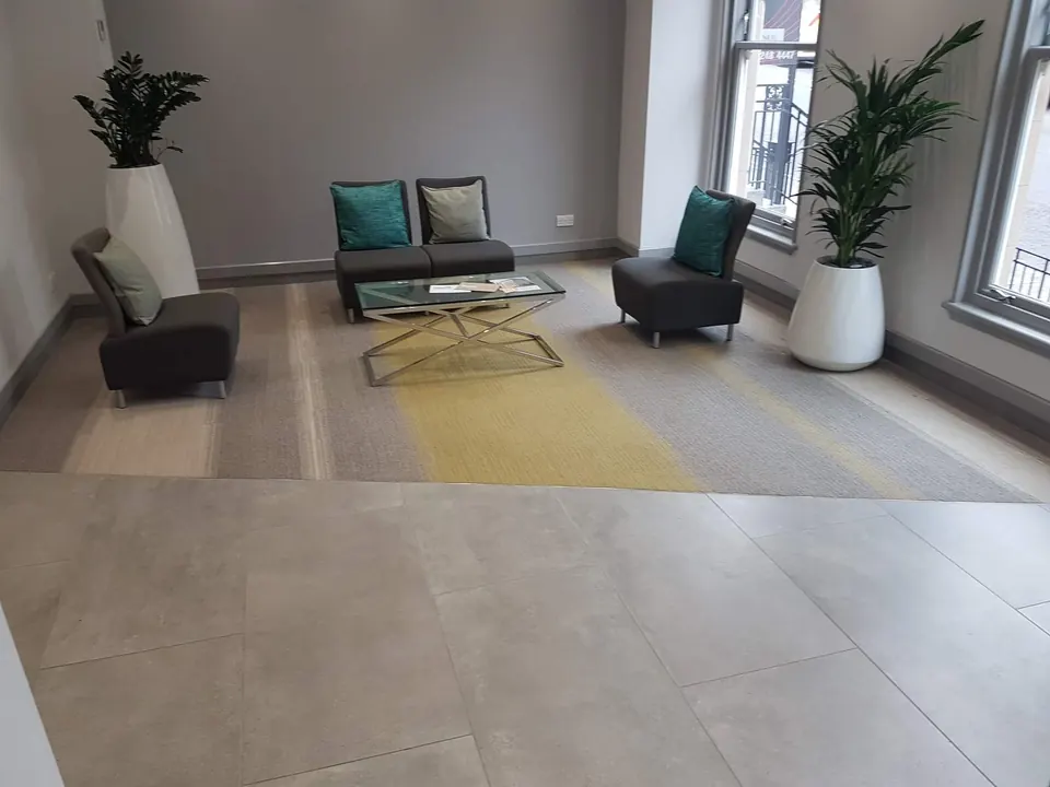 Office reception with striped carpet tiles meeting large stone-effect floor tiles