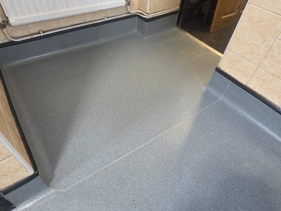 Grey safety flooring with welded cap and cove skirting in a commercial washroom