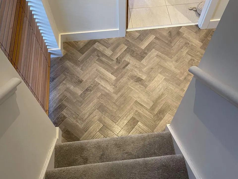Grey stair carpet leading down to a herringbone hallway floor